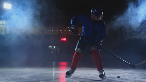 Professioneller-Eishockeyspieler-Mit-Schläger-Und-Puck-Bewegt-Sich-Auf-Luda-In-Schlittschuhen-Und-Helm-Auf-Dunklem-Hintergrund-Und-Rauch.-Dribbling-Mit-Dem-Puck-Eines-Jungen-Mannes-Auf-Der-Eisbahn